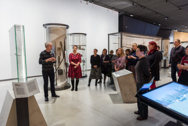 Muuseumi näitusesaalis seisab grupp külastajaid ringis, kuulamas giidi.